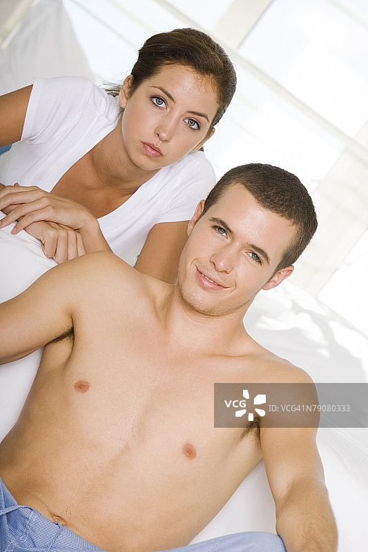 年轻男人坐在地板上，年轻女人躺在床上的肖像图片素材