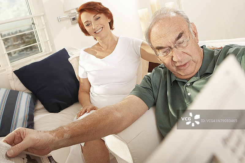 一位老年男人在看报纸，一位老年女人坐在他身后特写图片素材