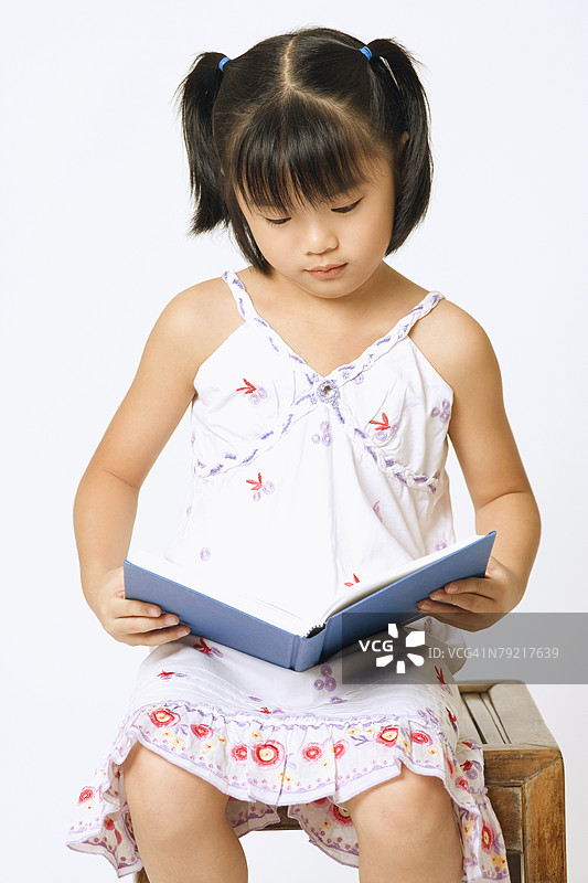 女孩坐在凳子上专心阅读一本书的特写镜头图片素材