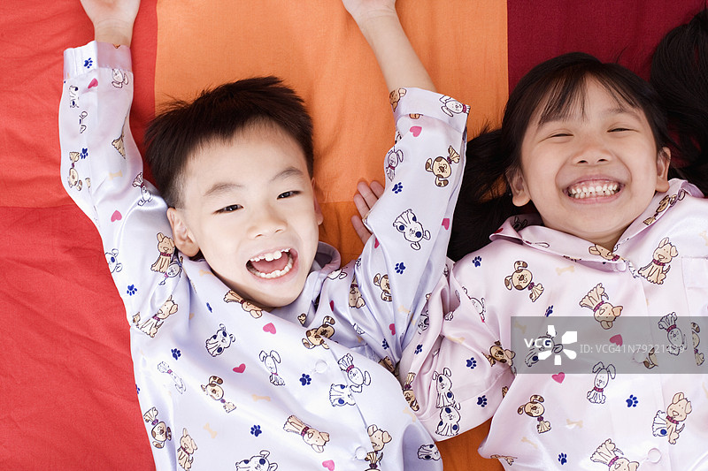 一个男孩和一个女孩躺在床上，面带愉快的笑容。图片素材