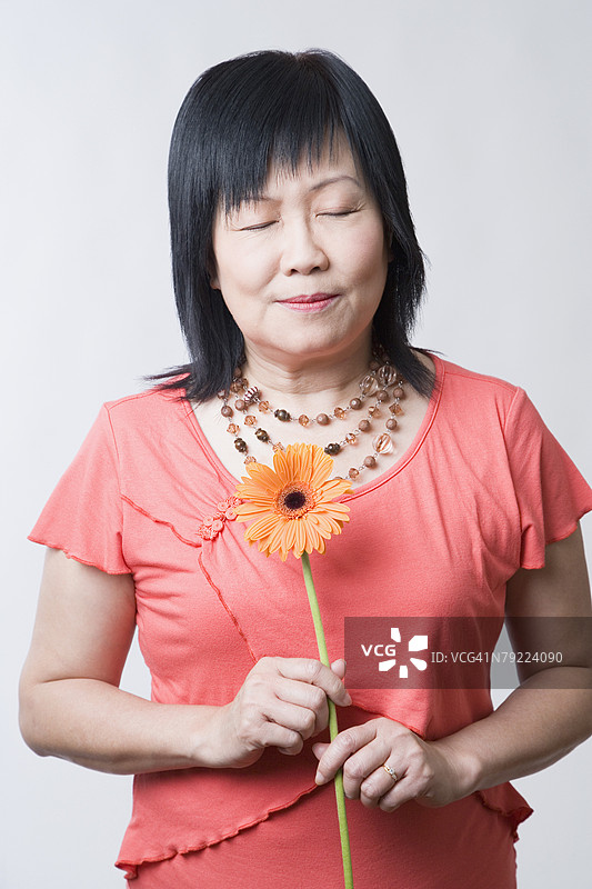 特写镜头：一位成熟的女性闭着眼睛，手中捧着一朵雏菊。图片素材