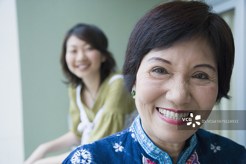 一位微笑的老年女性肖像，她的孙女站在她身后。图片素材