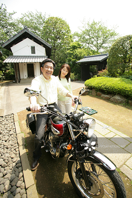 成熟男性坐在摩托车上，旁边有一位女性注视着他。图片素材