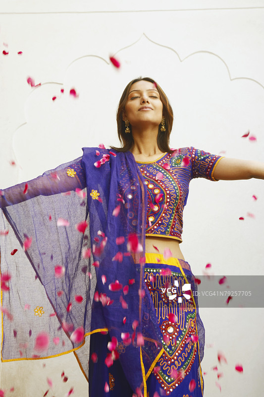 年轻女子站立，周围飘落玫瑰花瓣的特写镜头图片素材