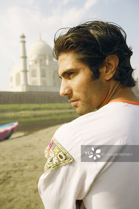 年轻男子背对着河岸，侧身望向一旁，背景是印度阿格拉的泰姬陵。图片素材