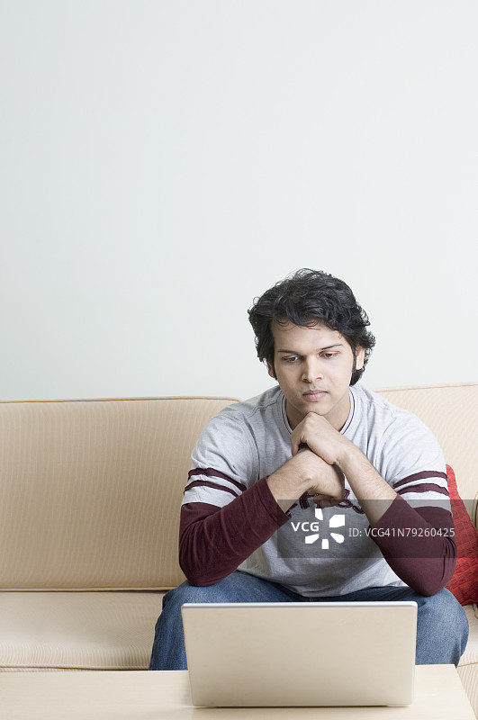 年轻女人坐在沙发上看笔记本电脑图片素材