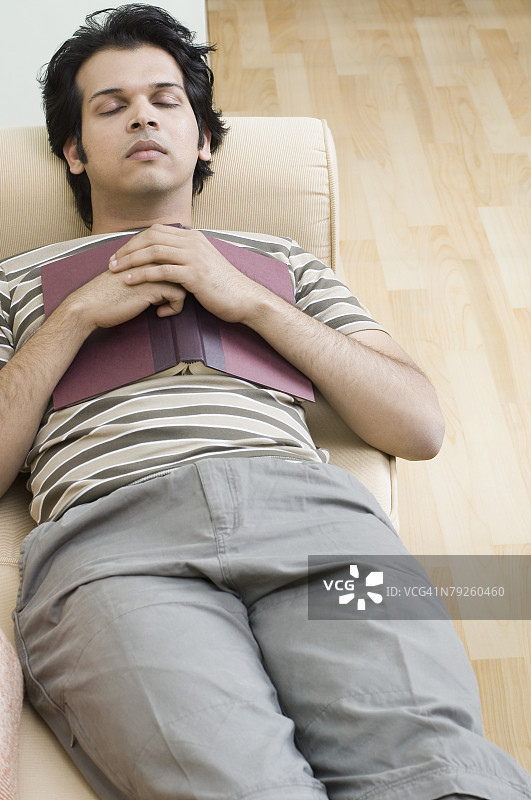 高角度拍摄：年轻男子躺在沙发上，胸前放着一本书图片素材