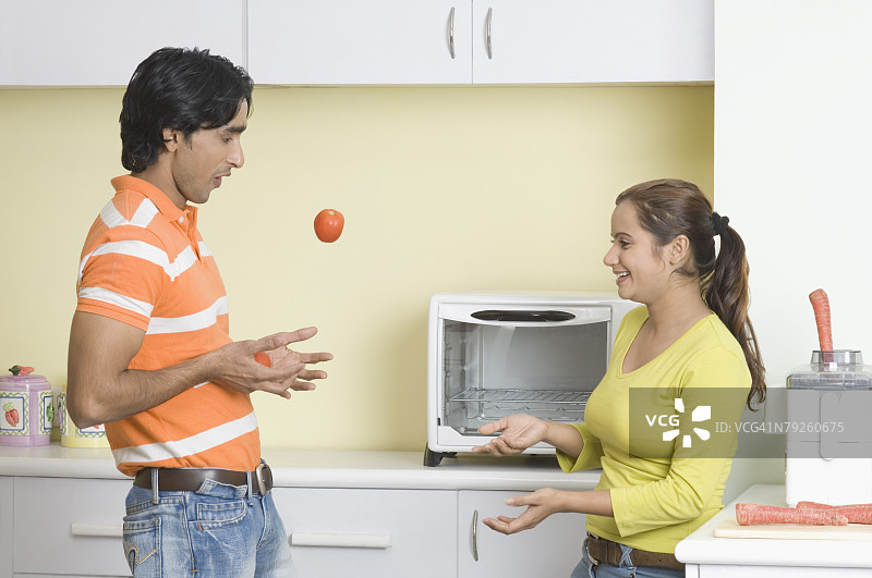 年轻情侣在厨房玩番茄侧面照图片素材