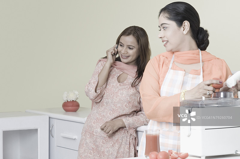 使用电动搅拌器，另一位女人在用手机交谈图片素材