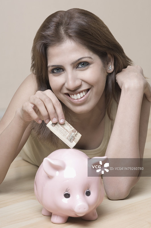 年轻女子往储蓄罐里放钱的肖像图片素材