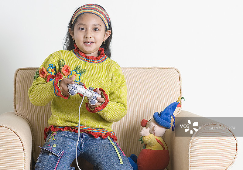 跪在扶手椅上玩电子游戏的女孩肖像图片素材