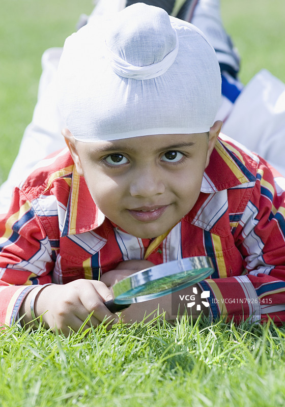 躺在草地上，拿着放大镜的男孩肖像图片素材