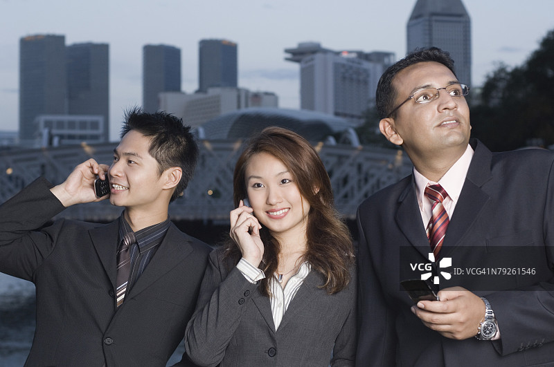 在新加坡，两位商人和一位女商人站在一起使用手机图片素材