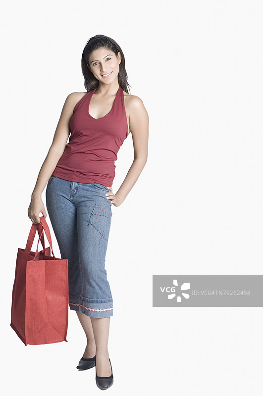 年轻女性手持购物袋，站立时一只手放在臀部上。图片素材