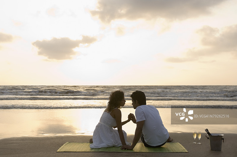 一对年轻夫妇手牵着手坐在野餐毯上的背影图片素材