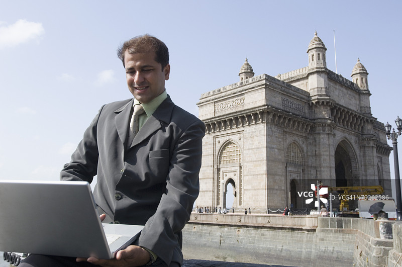 商人使用笔记本电脑，背景是印度孟买的印度门图片素材