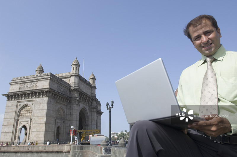 使用笔记本电脑微笑的商人，印度孟买印度门图片素材