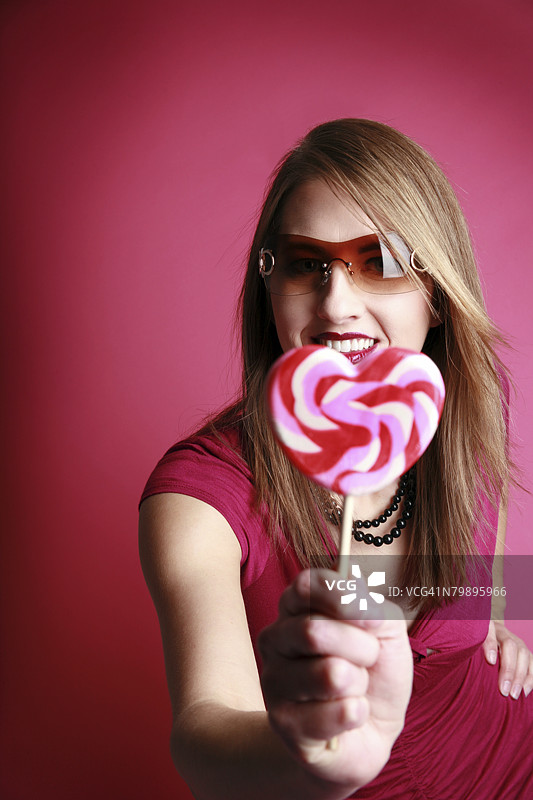 一位白人模特佩戴着太阳镜，手里拿着一个心形棒棒糖。图片素材