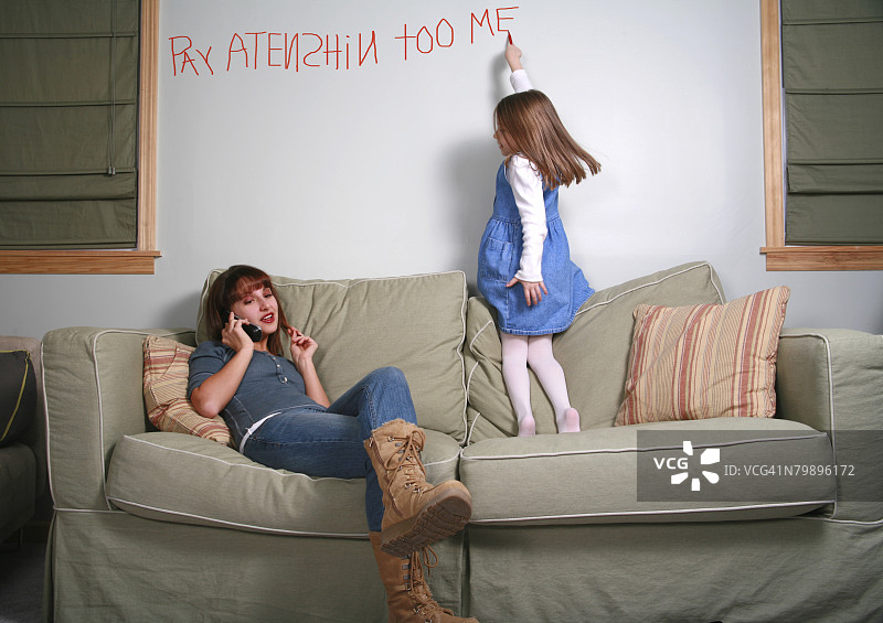 五岁女孩在墙上乱写乱画，保姆/年轻母亲在打电话图片素材