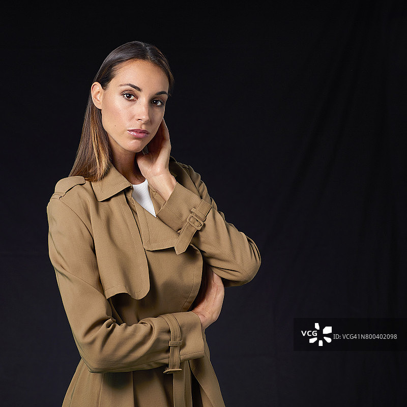 穿着风衣，手放在脸上的年轻女人图片素材