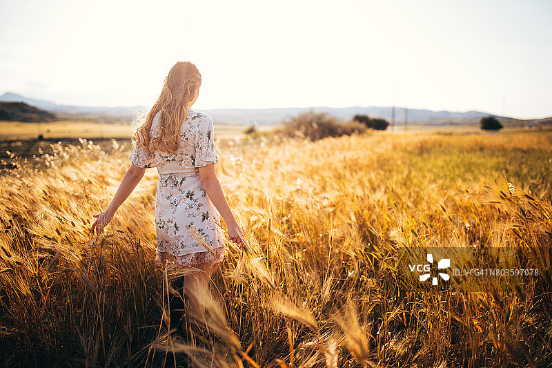 复古风格的女孩站在日落时分的金色麦田里图片素材
