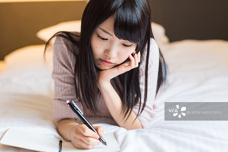 年轻女人在卧室的床上写日记图片素材