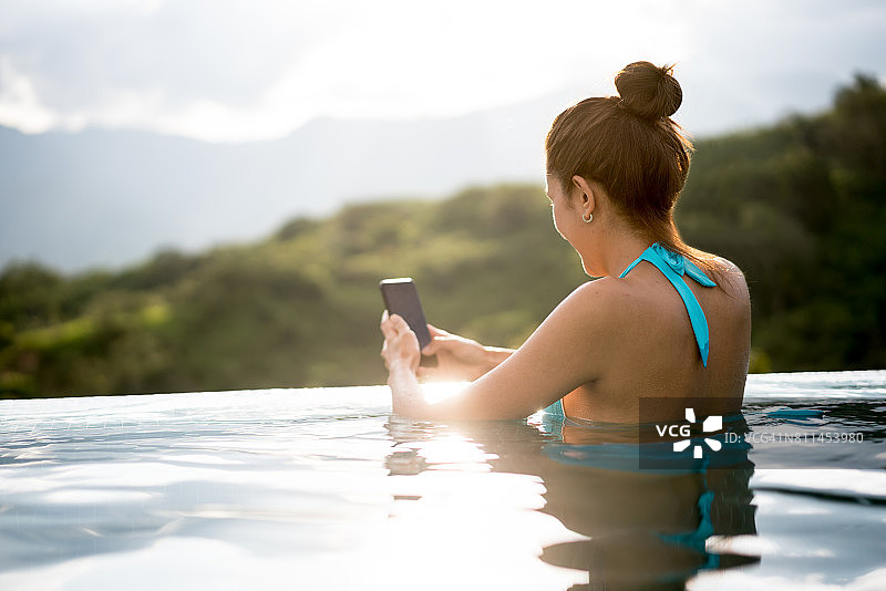 女人在游泳池放松时发短信图片素材