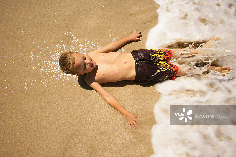男孩躺在海滩的水里图片素材