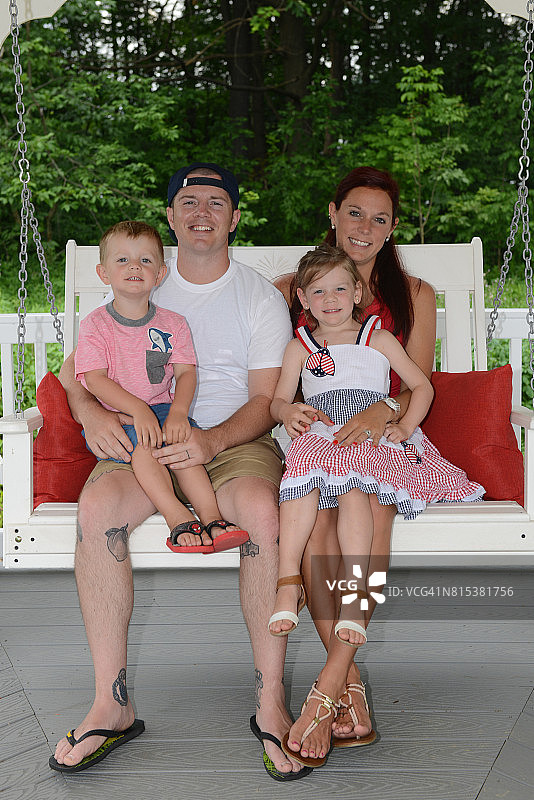 父母抱着微笑的幼儿子女坐在白色长椅上（肖像照）图片素材