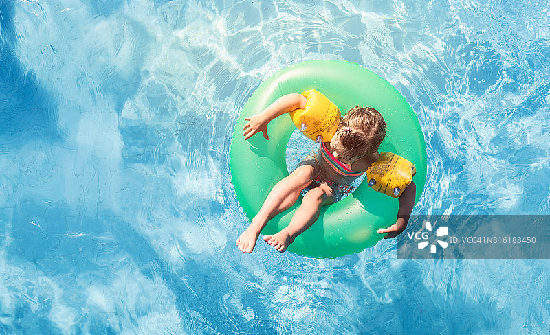 快乐女孩在游泳池里戴着游泳圈漂浮图片素材