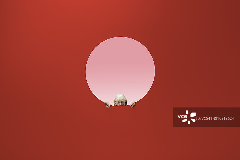 女人从彩色墙壁的圆形开口中探出头图片素材