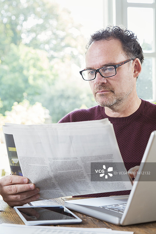 在厨房使用笔记本电脑和阅读报纸的商人图片素材