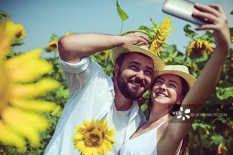 情侣在向日葵田中戴着帽子自拍图片素材