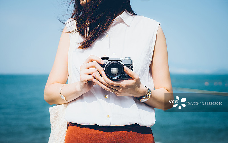 女孩在阳光明媚的海滩用老式胶片相机拍照图片素材