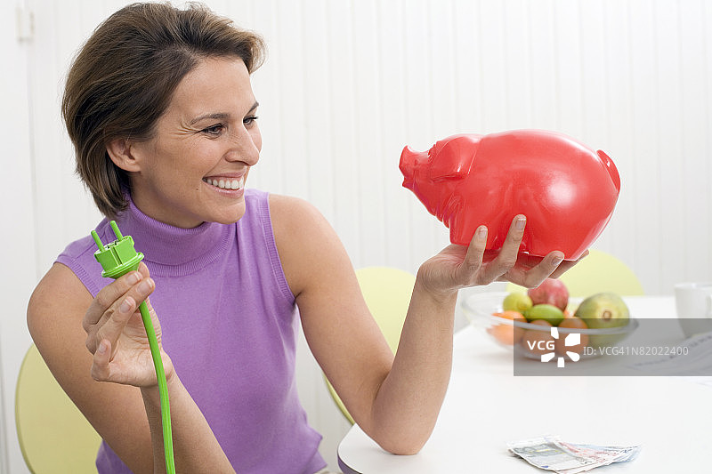 女人手持绿色插头和储蓄罐图片素材