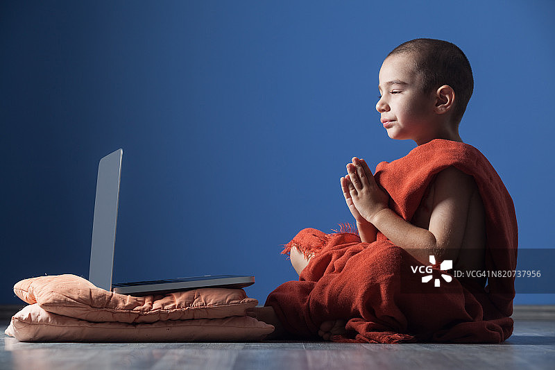 光头小男孩身穿橙色僧袍在电脑前冥想图片素材