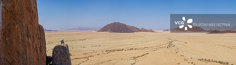 沙漠岩石上手持双筒望远镜的男人全景图片素材