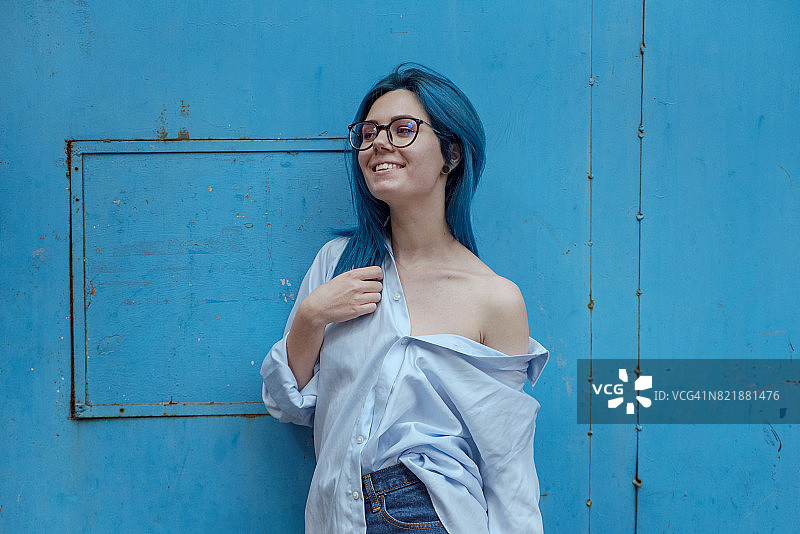 鲜艳色彩：蓝发女子在蓝色墙壁旁微笑图片素材