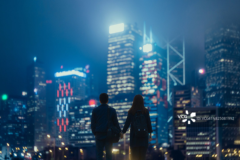 情侣手牵手漫步在灯火辉煌的城市夜景中图片素材