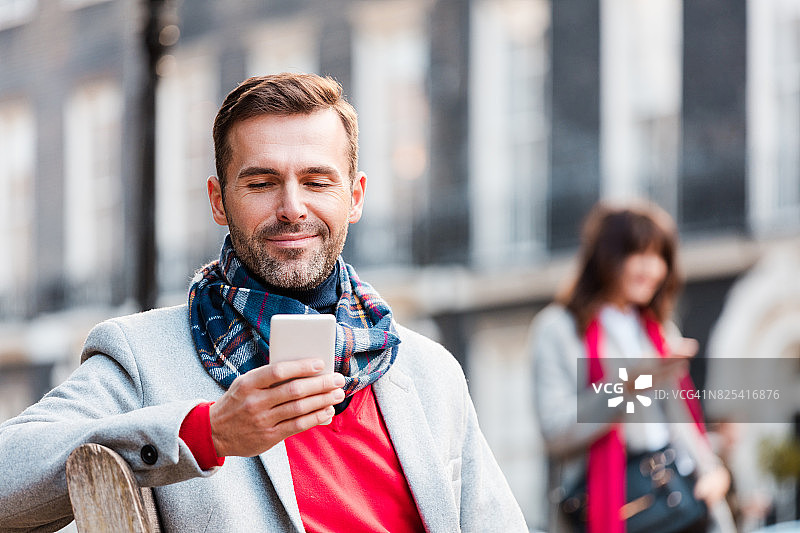 坐在长椅上使用智能手机的微笑男人图片素材
