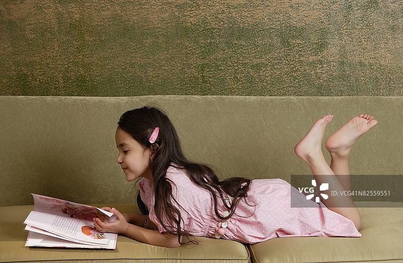 女孩赤脚在沙发上看故事书图片素材