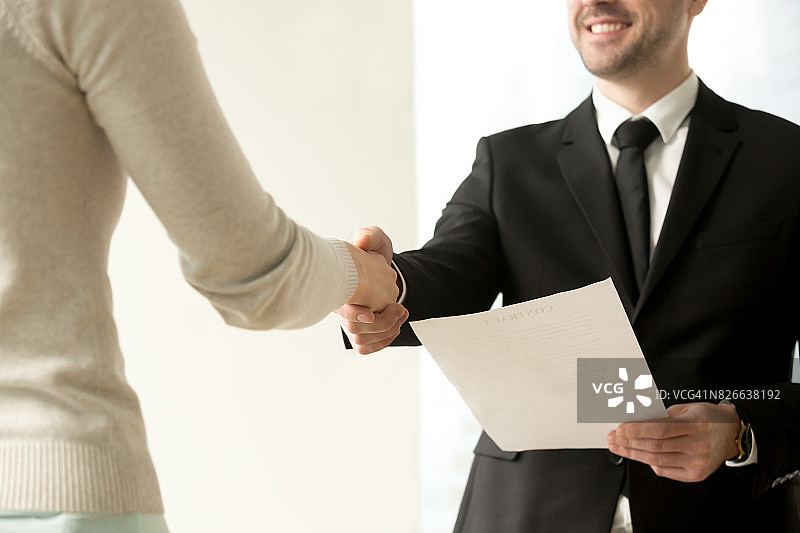 雇佣握手特写：雇主与新员工握手并提供合同图片素材