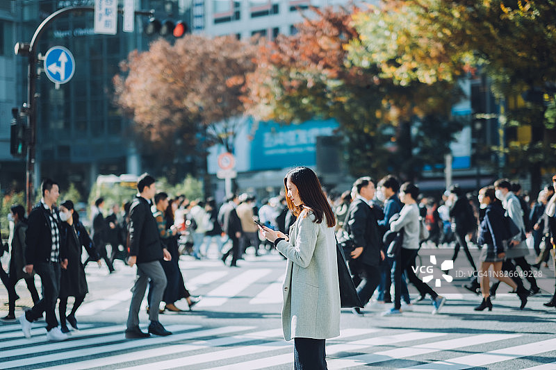 在东京繁忙的街道上使用智能手机的年轻女商人图片素材