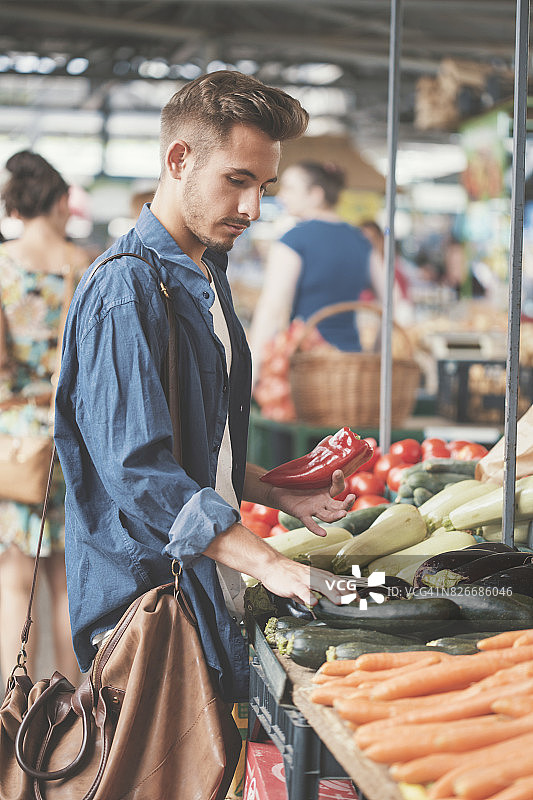 拿着红辣椒并拿起茄子的年轻男人图片素材