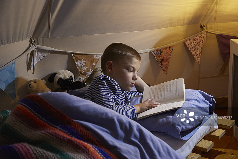 男孩晚上在帐篷里看书图片素材