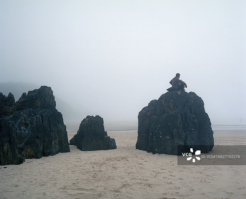 男子坐在俄勒冈海岸的岩石上图片素材