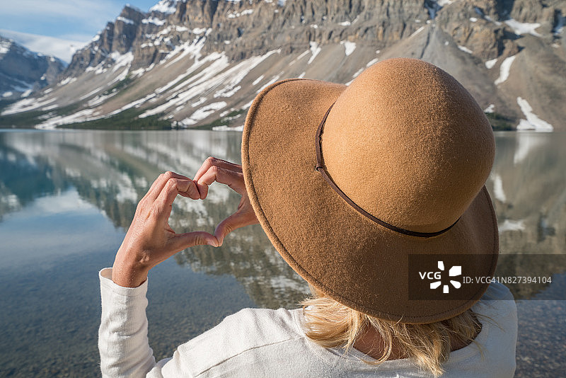 年轻女子在山间湖泊上手指比心图片素材