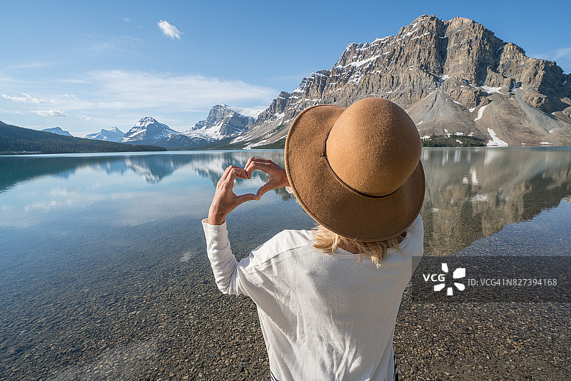 年轻女子在山间湖泊上手指比心图片素材