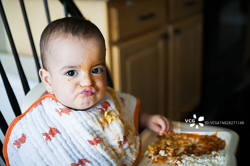 12个月大的异卵双胞胎男婴吃东西时嘟着嘴，满脸都是图片素材