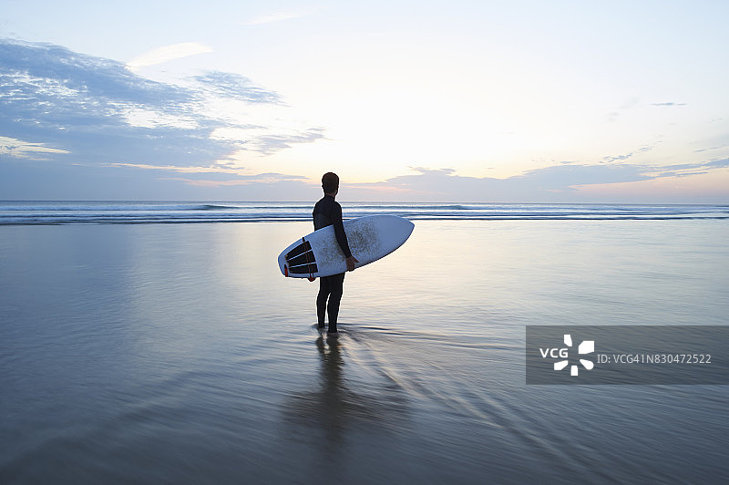 冲浪者拿着冲浪板在黄昏时眺望大海图片素材